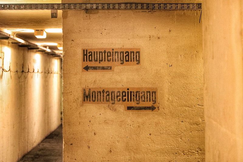 Wegweiser Haupteingang und Montageeingang an einer Bunkerwand